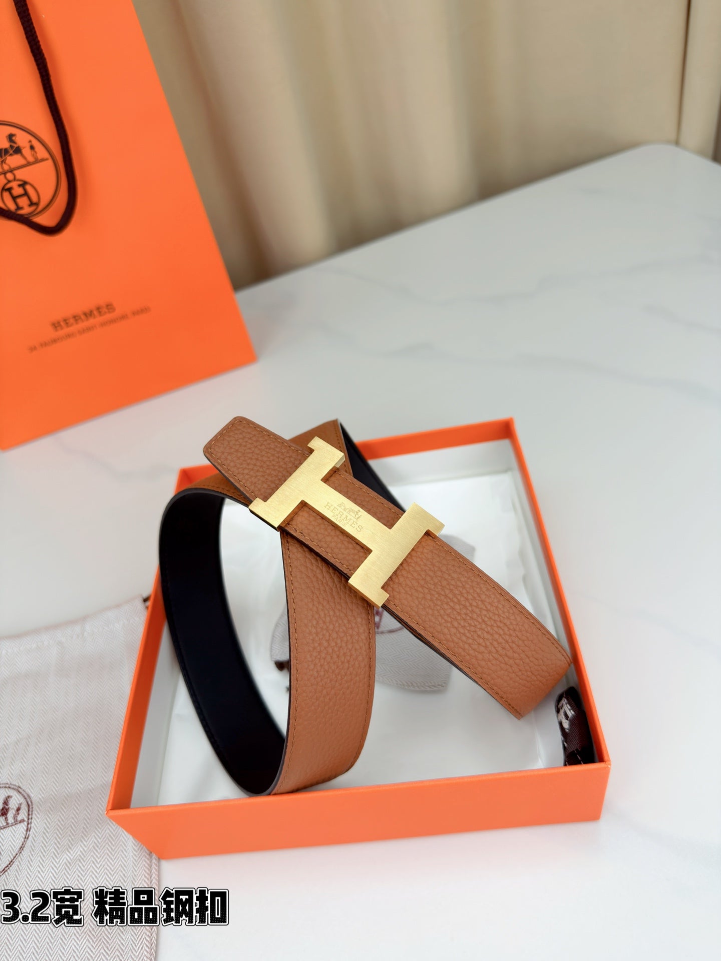 Brown leather belt with gold H buckle displayed with the strap looped and secured.