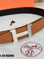 Brown leather belt close-up with gold H buckle and stitched edge detailing.