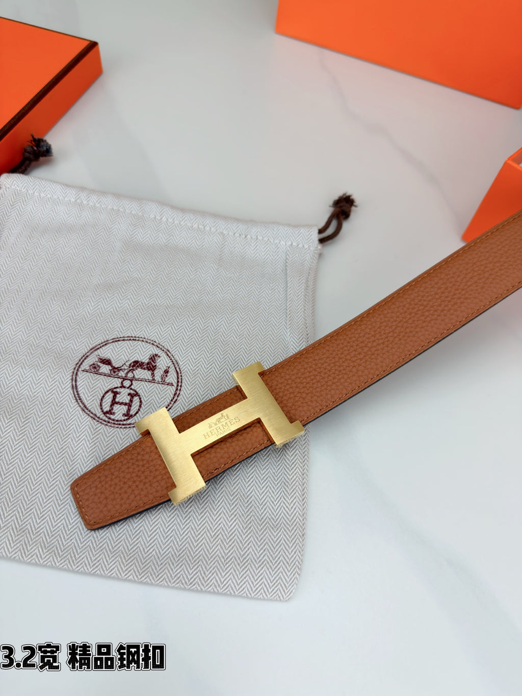 Brown leather belt angled close-up with gold H buckle and strap end detail.