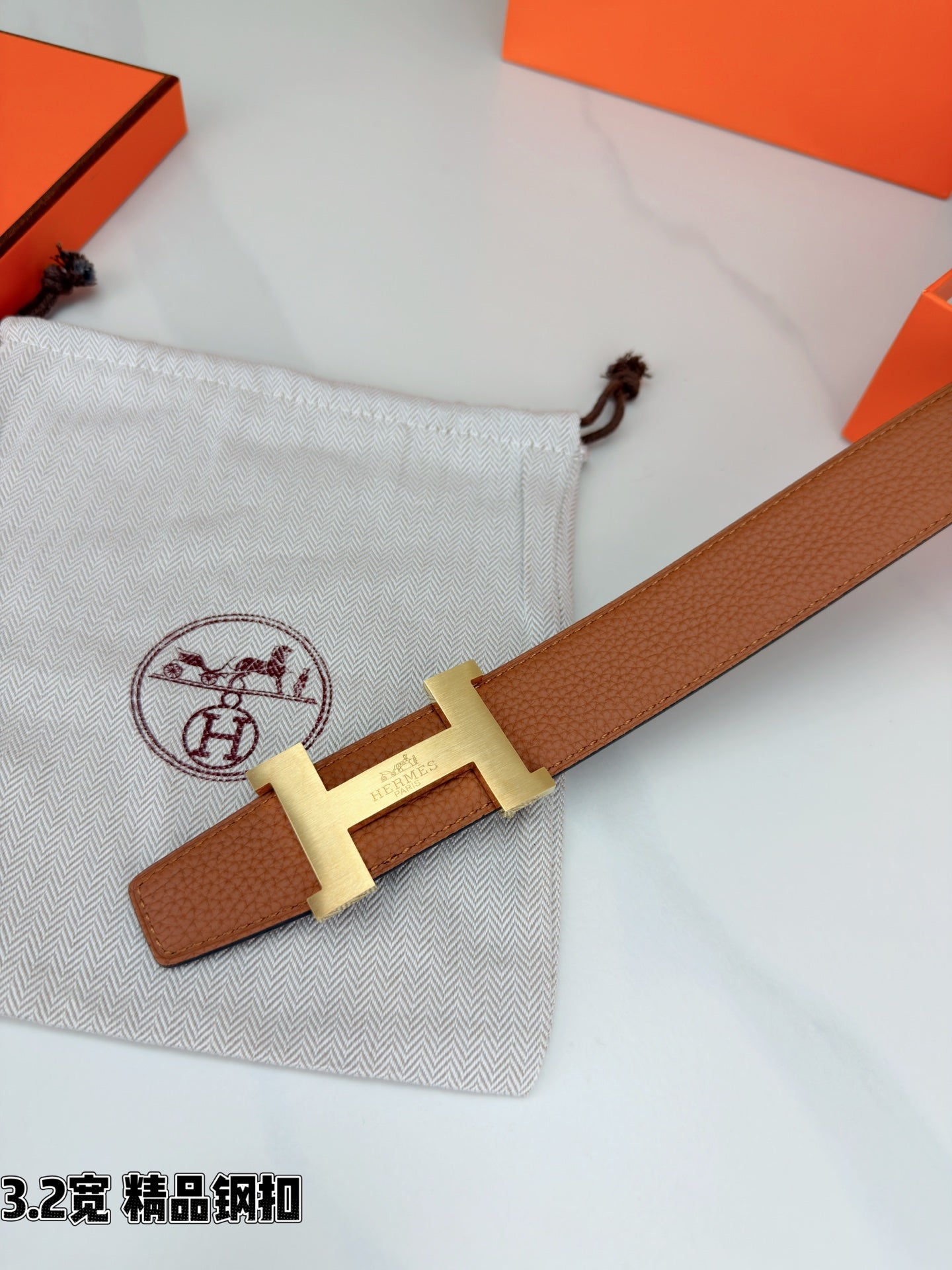 Brown leather belt angled close-up with gold H buckle and strap end detail.