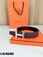 Dark brown leather belt with gold-tone H buckle, resting on gift box.