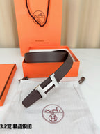 Dark brown leather belt with gold-tone H buckle on white dust bag.