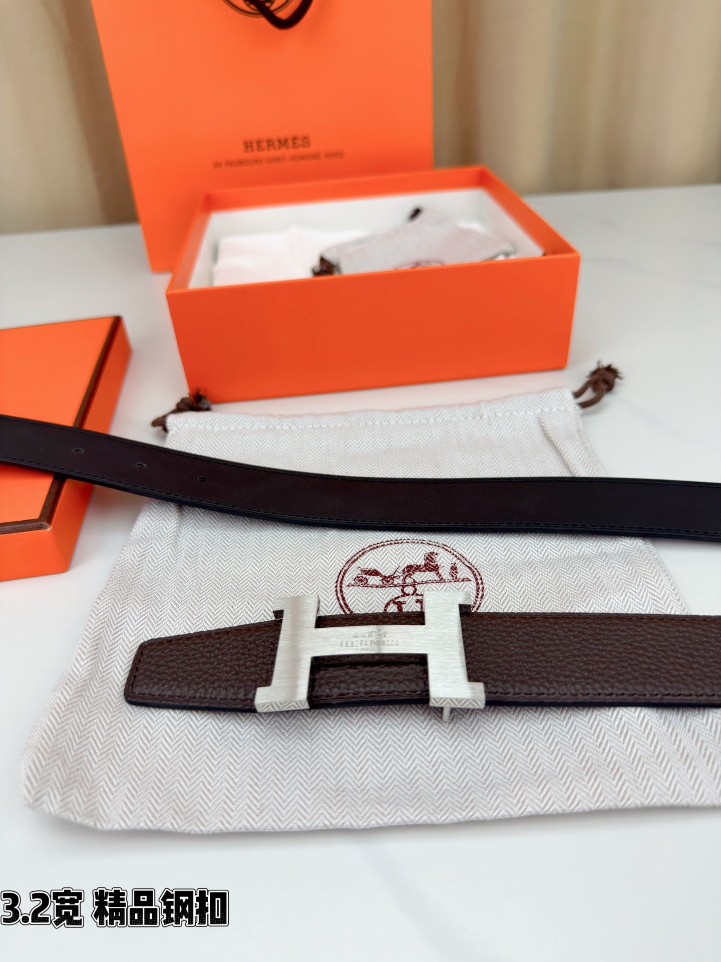 Dark brown leather belt with gold-tone H buckle laid on white fabric pouch.