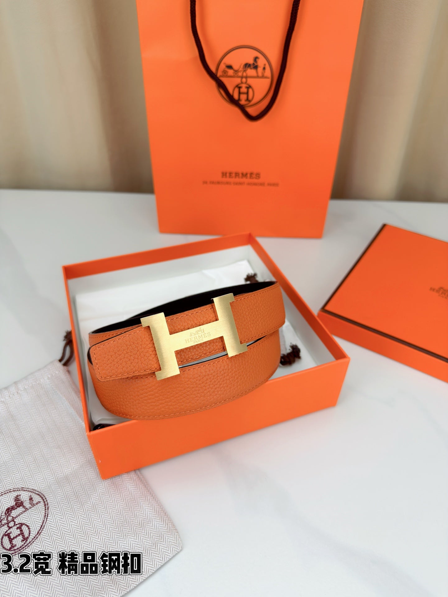 Orange leather belt with metal H buckle displayed in open gift box