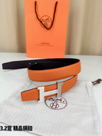 Orange leather belt with metal H buckle and black underside, resting on fabric