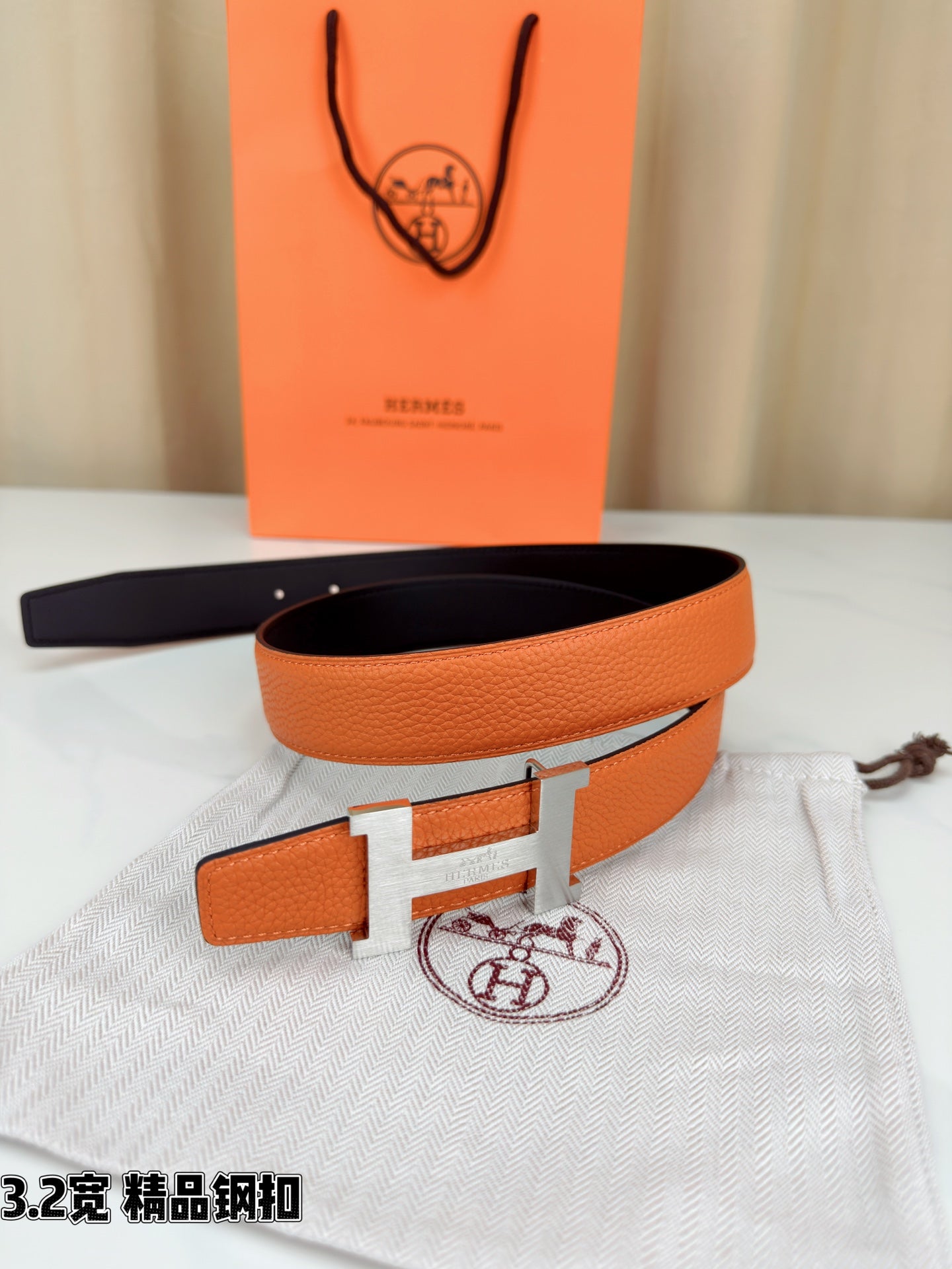 Orange leather belt with metal H buckle and black underside, resting on fabric