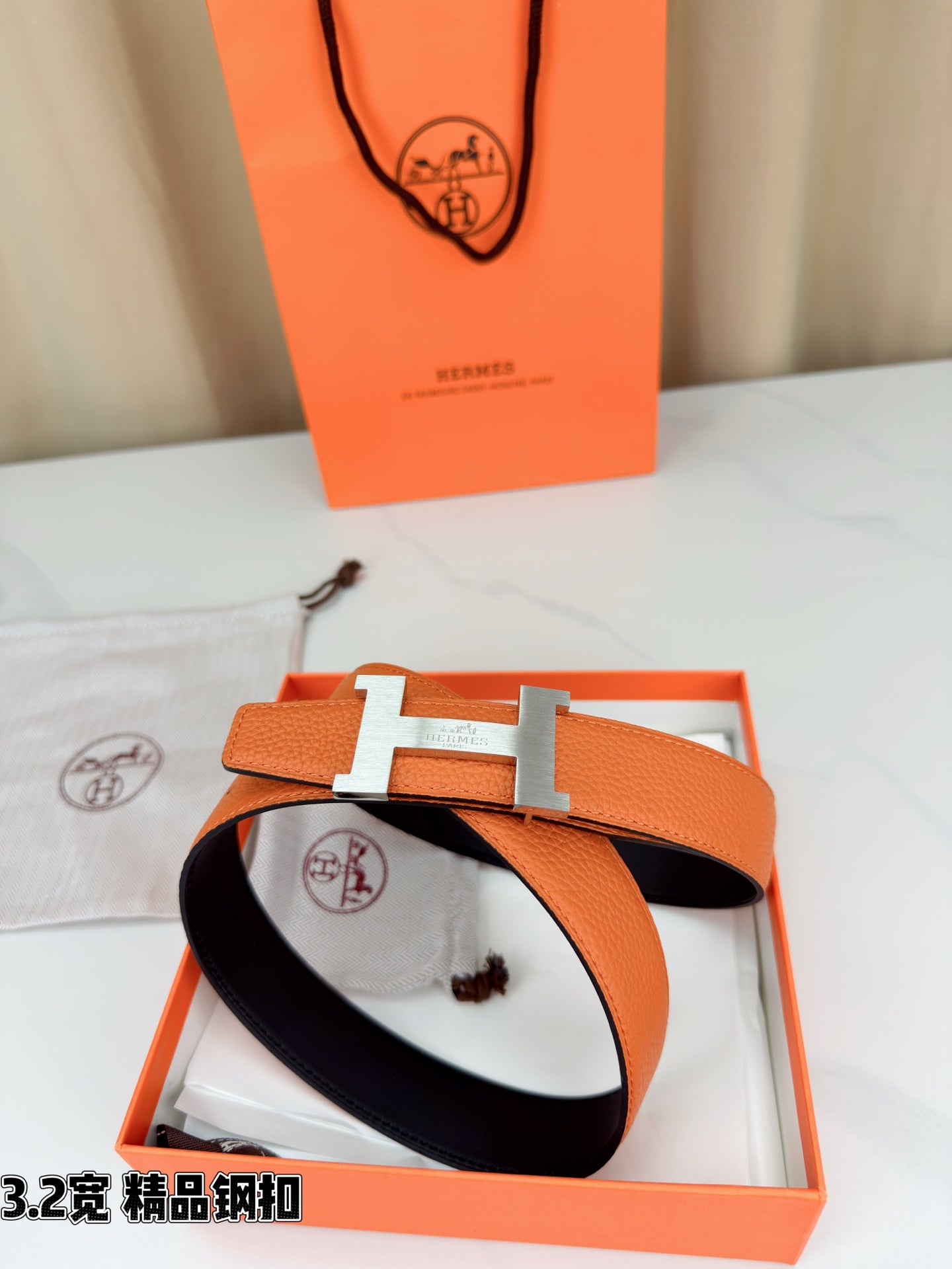 Orange leather belt with metal H buckle in open gift box, with dust bag
