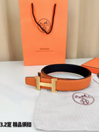 Orange leather belt with metal H buckle, laid on white cloth with box