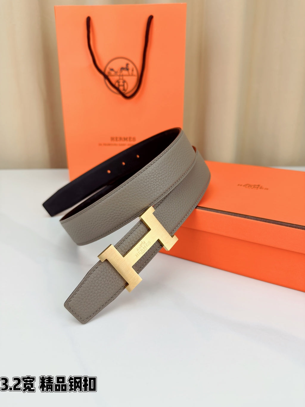 Grey leather belt with gold-tone H buckle, strap laid over box