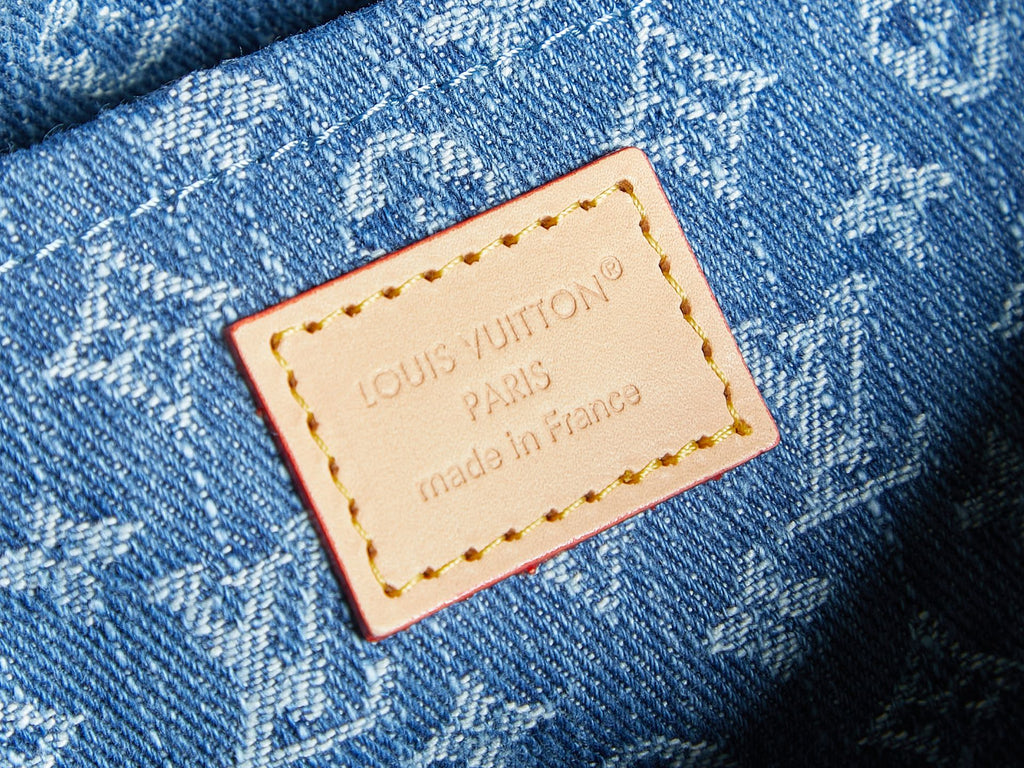 Close-up of Louis Vuitton label on blue monogram denim bag.