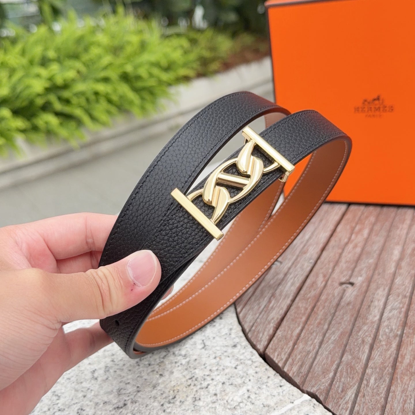 Black leather belt with gold buckle, held in hand; tan lining visible