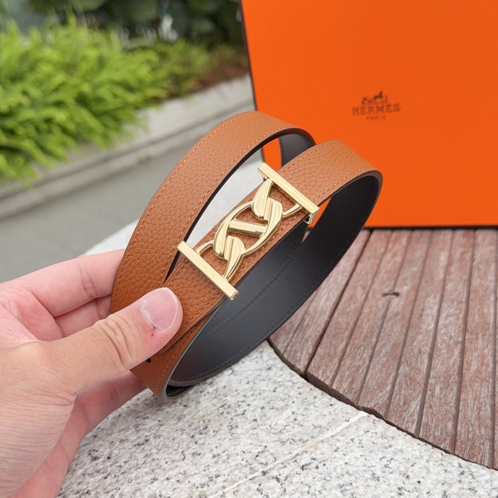 Hermes belt close-up held in hand: tan leather strap with gold-toned buckle
