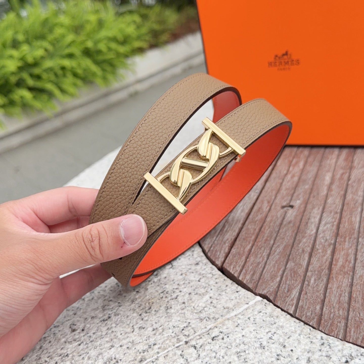 Leather belt with tan strap and gold logo buckle, held in a hand