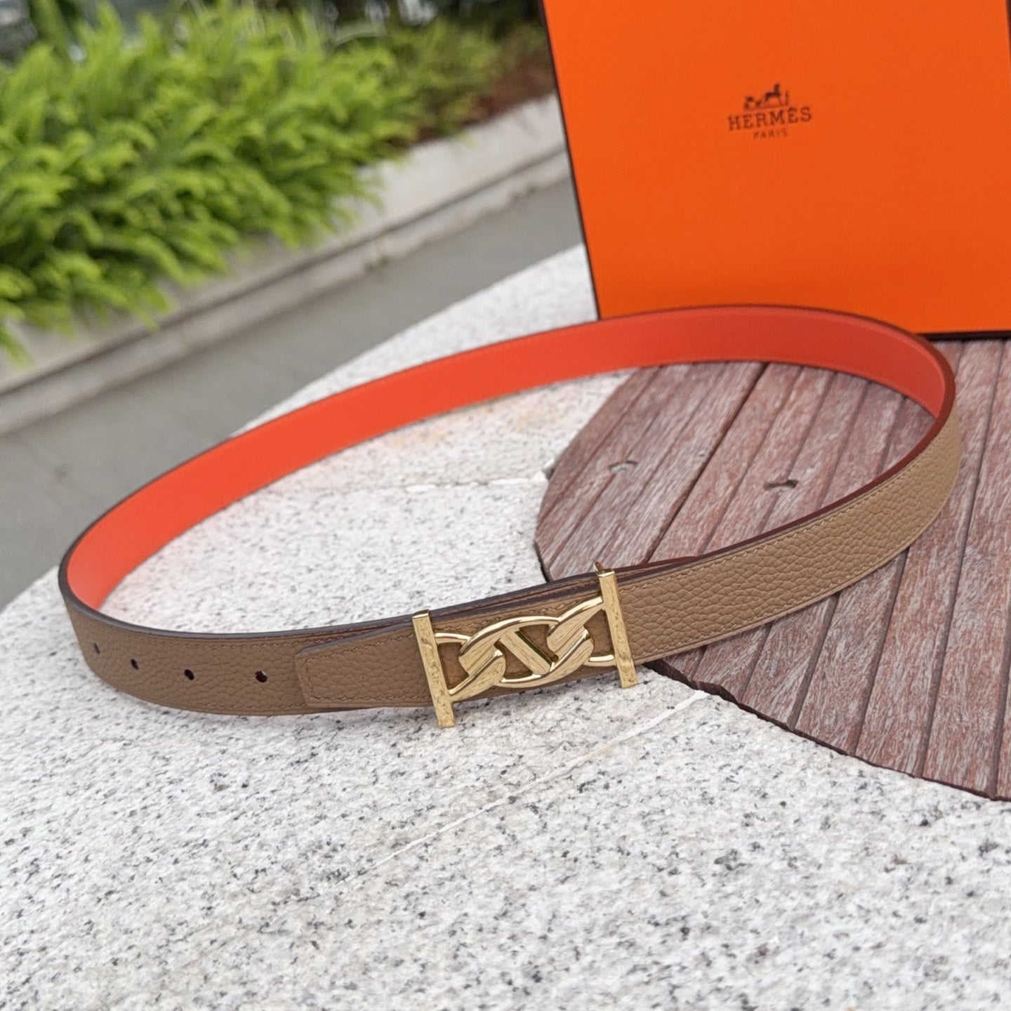 Leather belt with tan strap and gold buckle, resting on a stone surface
