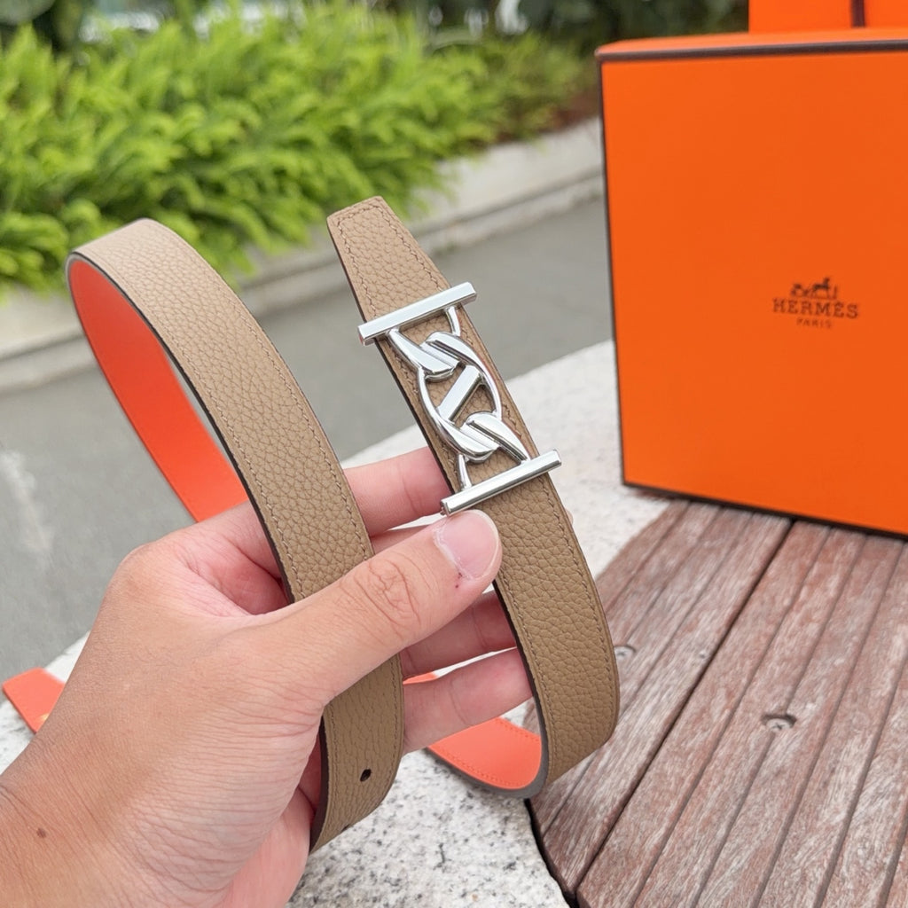 Leather belt held in hand: tan strap with silver buckle and orange underside