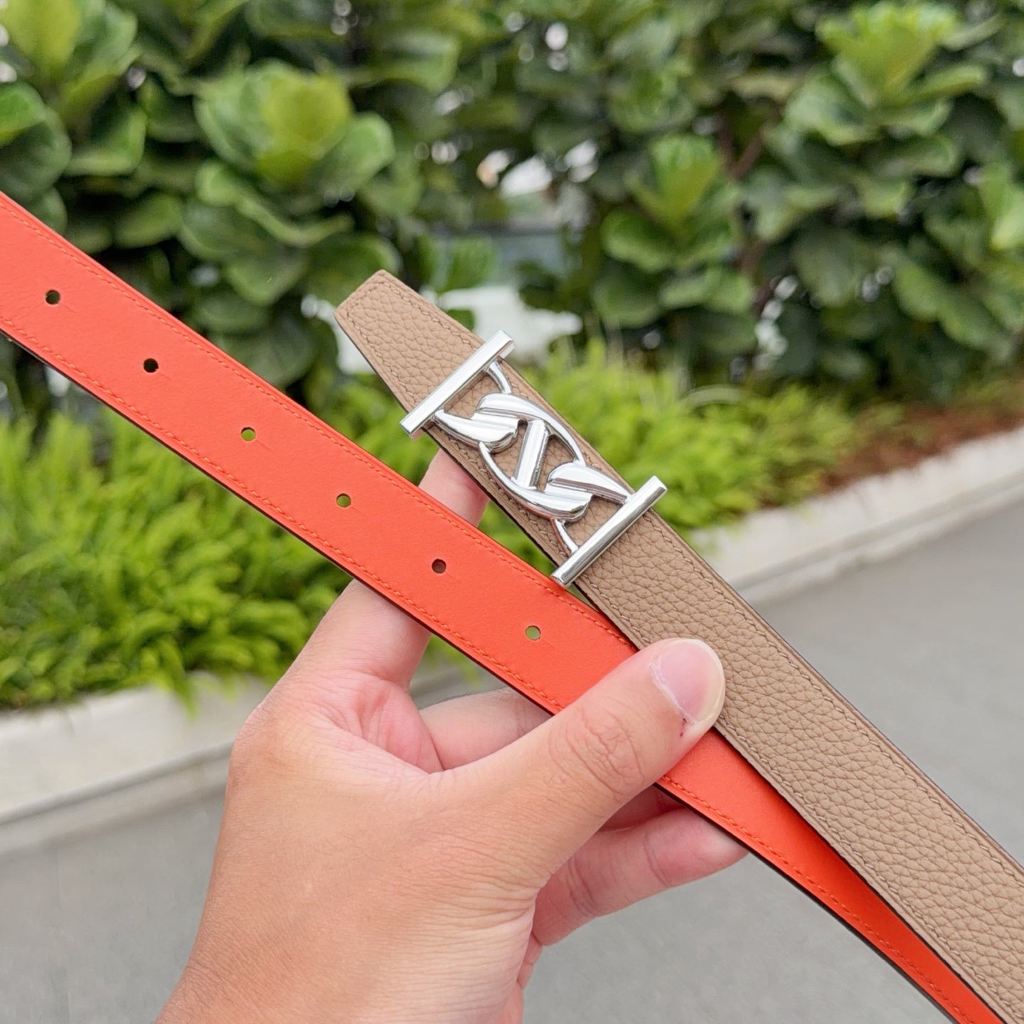Leather belt close-up: orange leather side with stud holes and silver buckle