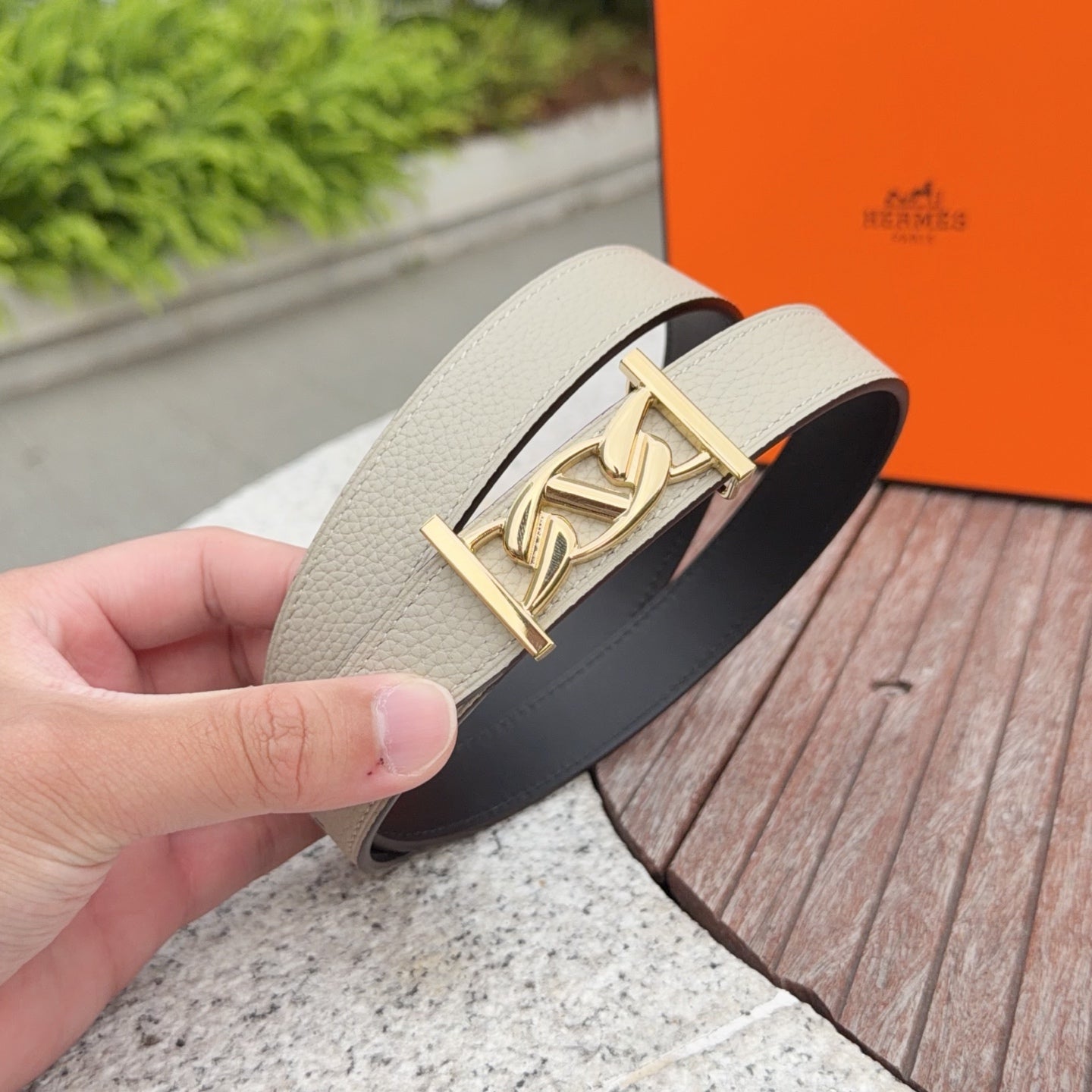 Beige leather belt close-up with gold-tone clasp buckle and dark underside