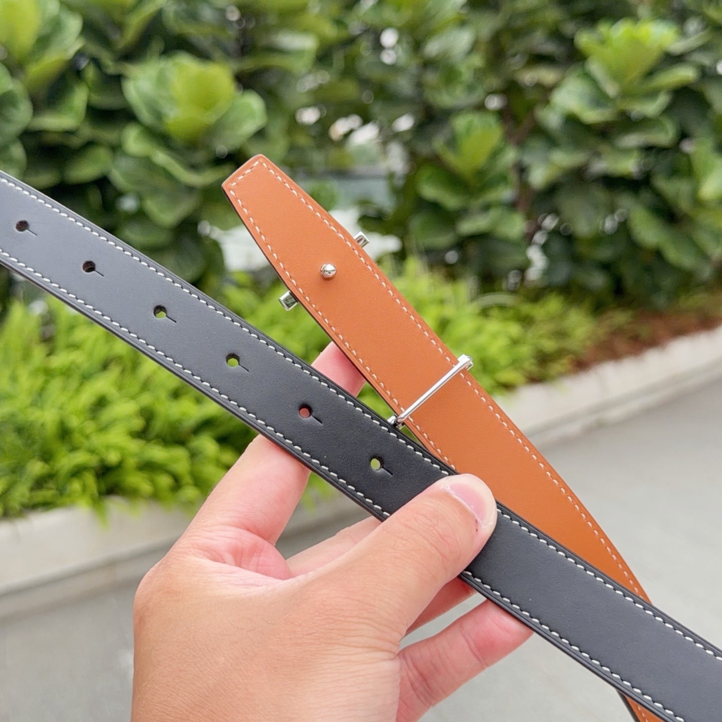 Leather belts in dark gray and tan, each with punched holes and white stitching