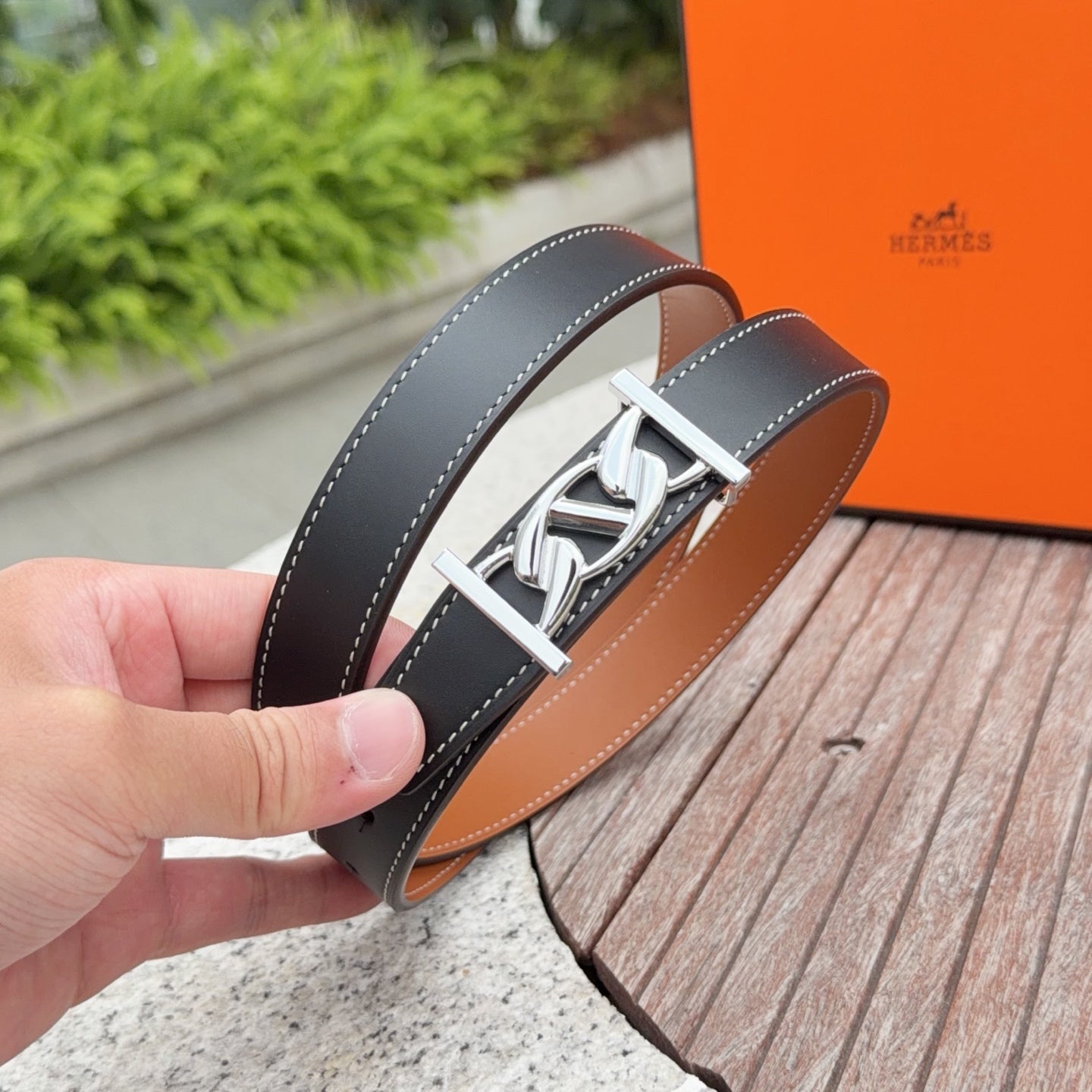 Dark leather belt with silver H-style buckle, hand-held close-up