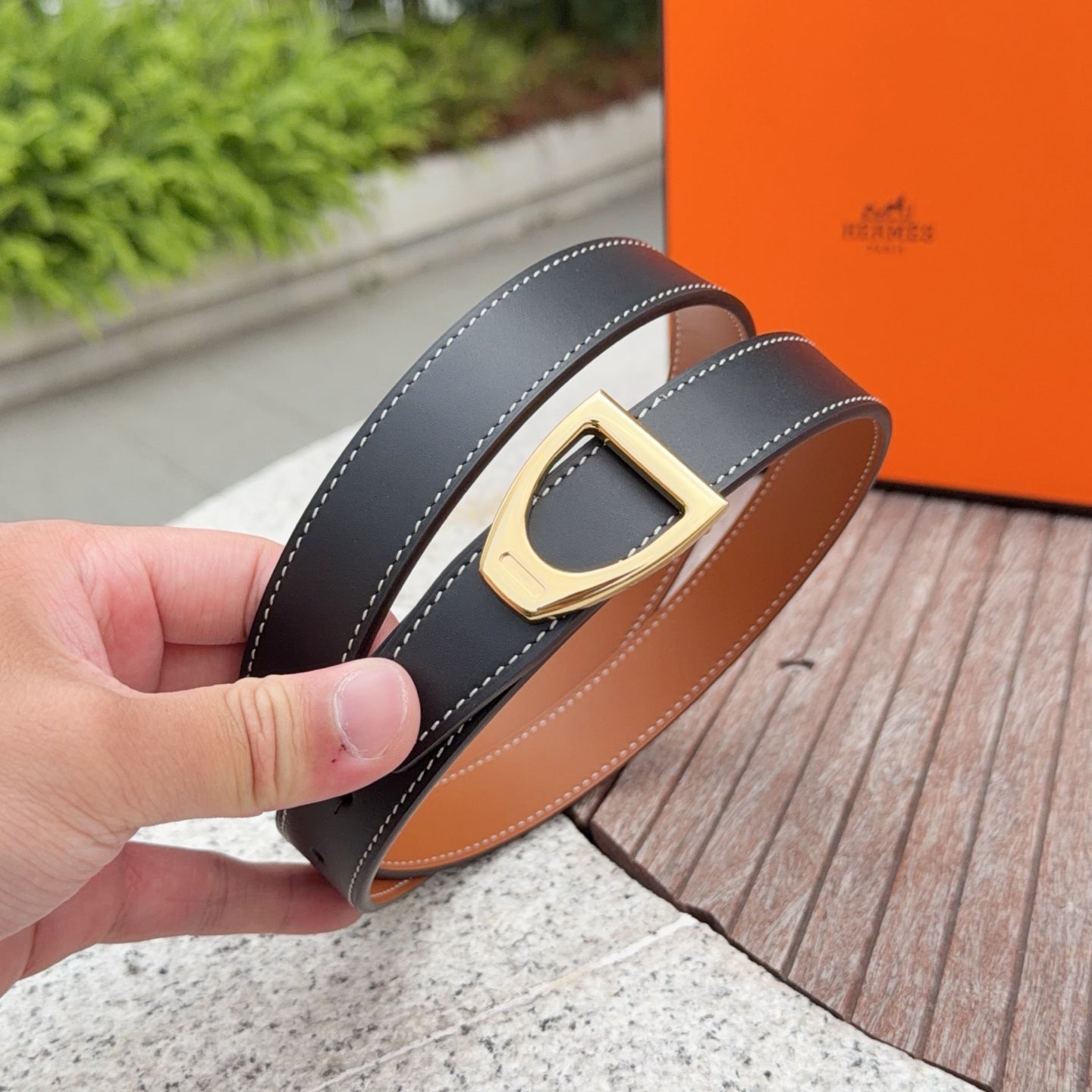 Leather belt with dark strap, gold buckle, and tan underside shown in hand