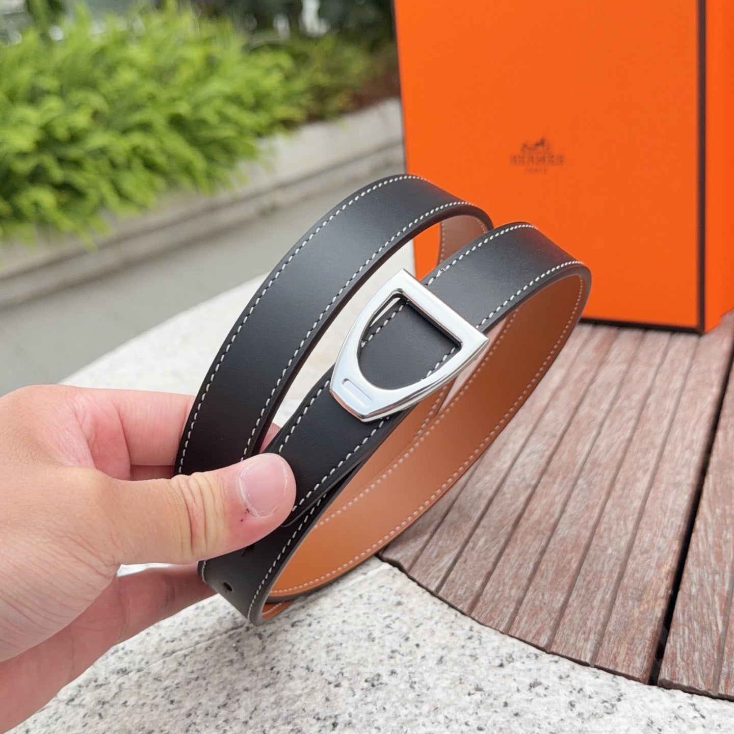 Hermes belt held close-up with silver buckle, dark strap and tan lining