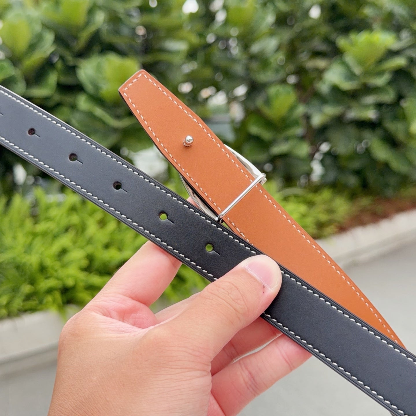 Hermes belt showing punched holes, dark leather strap with tan keeper