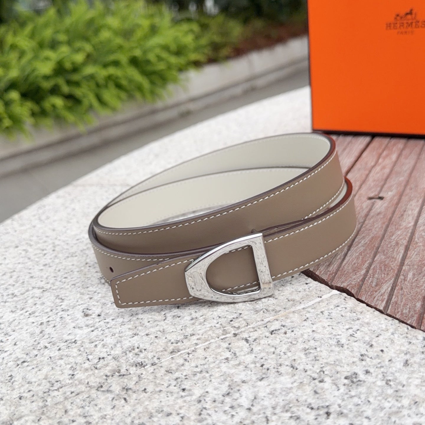 Hermes belt with light taupe strap and silver-tone buckle in a curved close-up