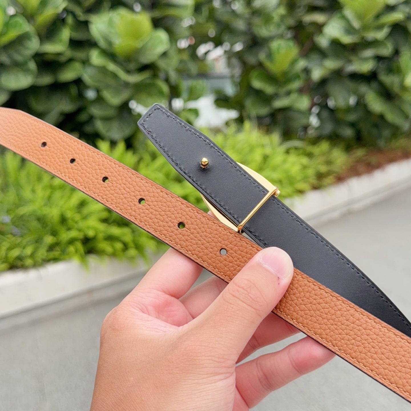 Tan leather belt with punched holes; gray belt with gold buckle behind.