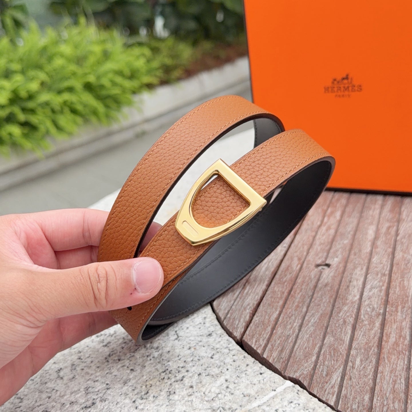Tan leather belt with gold buckle and black lining, shown in close-up.