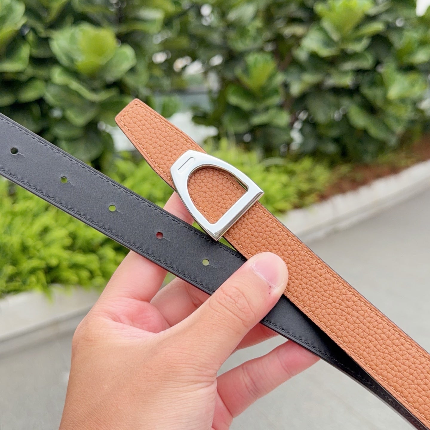 Leather belt with orange-brown strap and silver buckle over dark gray belt strap