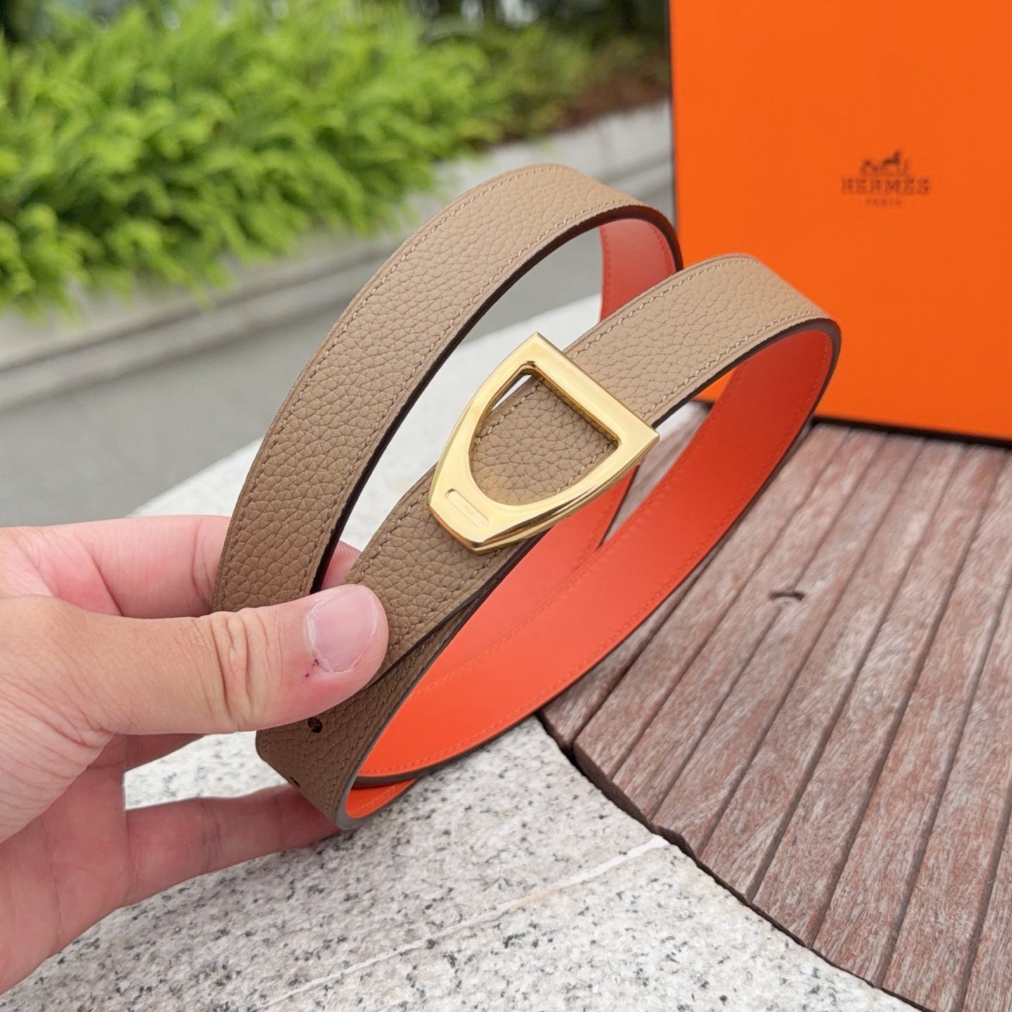Tan leather belt with gold buckle and orange lining, held in a hand for detail