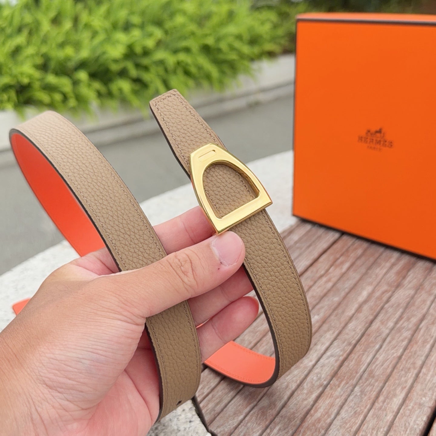 Tan leather belt with gold-tone rectangular buckle and orange underside, held upright
