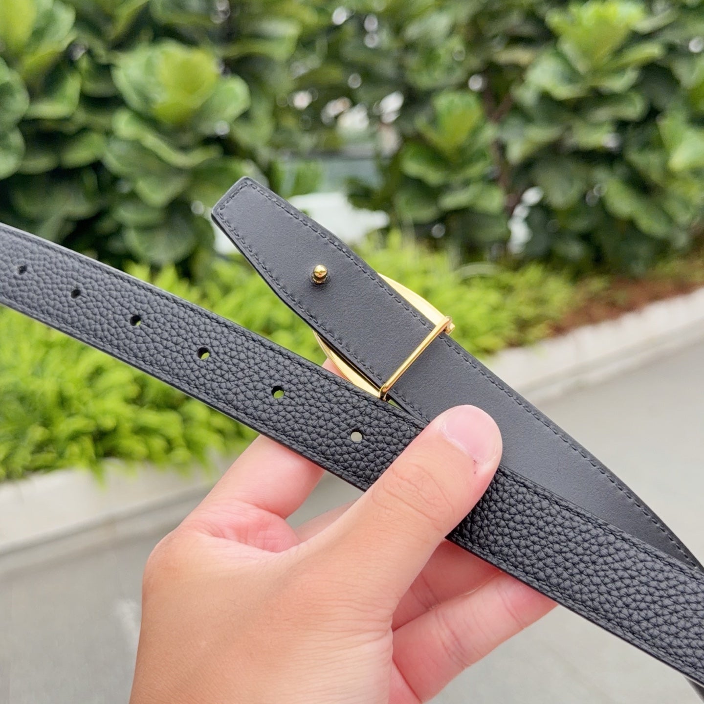 Black leather belt with gold-tone buckle and small punched holes, close-up