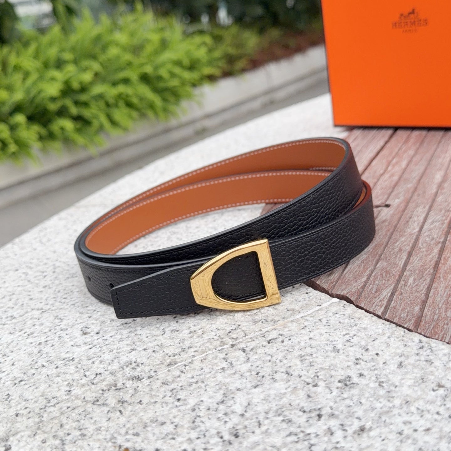 Leather belt with black strap and gold buckle, tan inner side and edge stitching