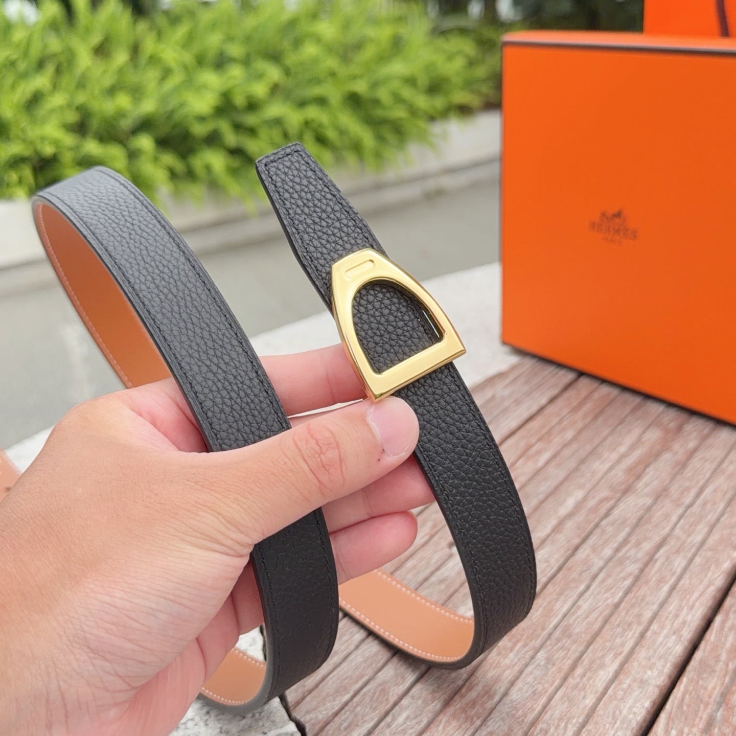 Leather belt on hand: black strap with gold buckle and tan lining