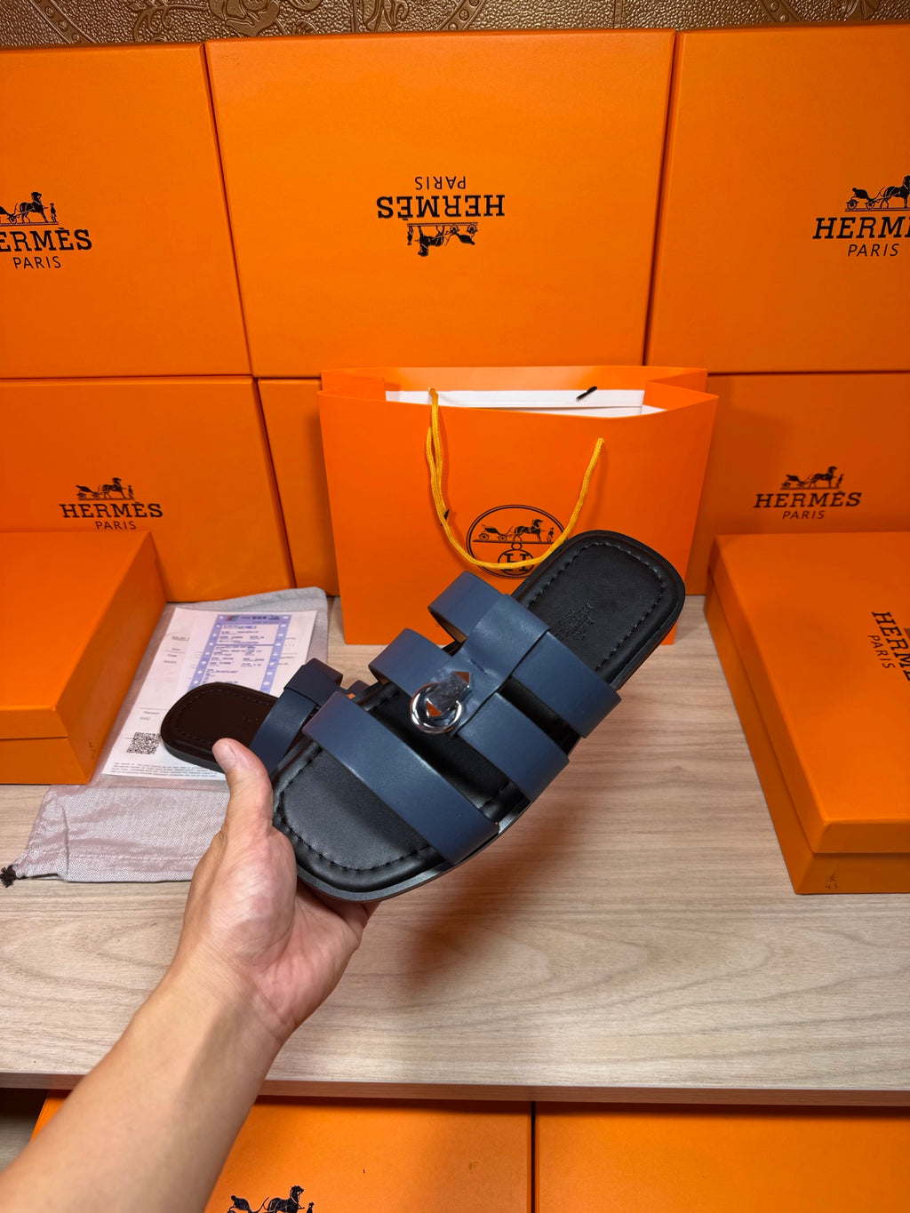 Hand holding dark blue leather slide sandals with two buckled strap bands