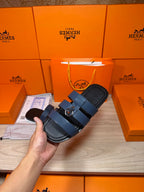 Hand holding dark blue leather slide sandals with two buckled strap bands