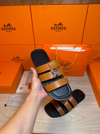 Hermes slide sandals shown close-up on tan straps with silver buckle hardware.