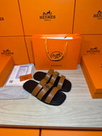 Hermes leather sandals with wide tan straps and silver buckle on dark sole.
