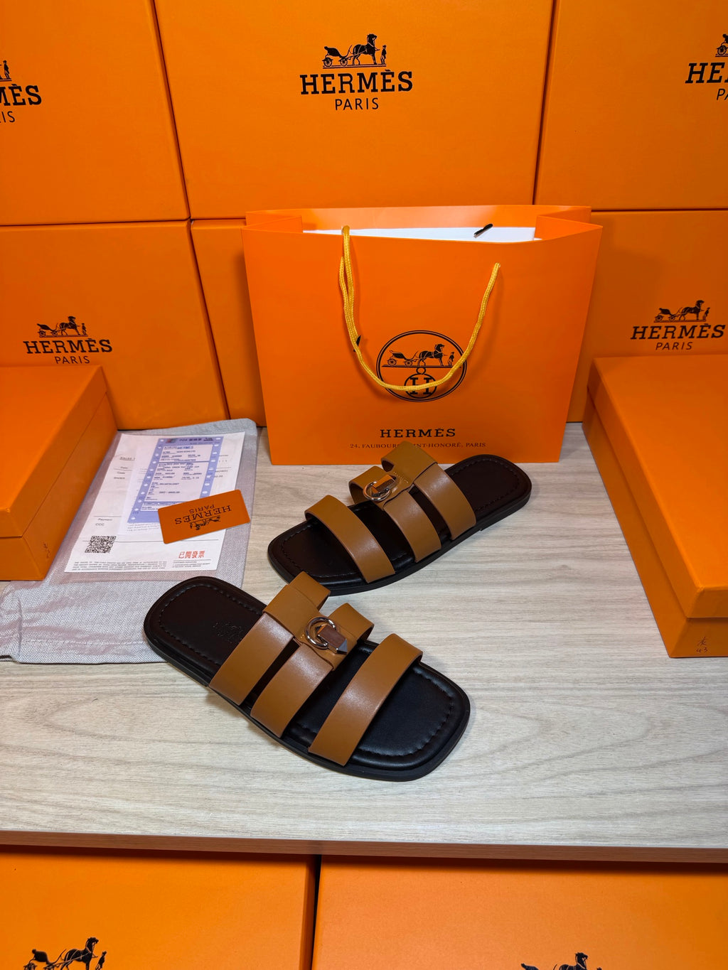 Hermes sandals featuring tan strap bands and a silver buckle over dark footbed.