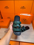 Hermes green leather slide sandal held close-up, two straps with silver buckle