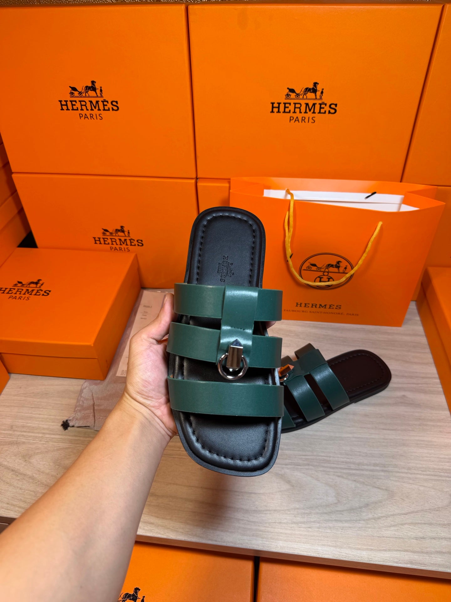 Hermes green leather slide sandal held close-up, two straps with silver buckle