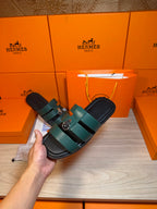 Hermes green leather slide sandal held in hand, two straps with silver buckle