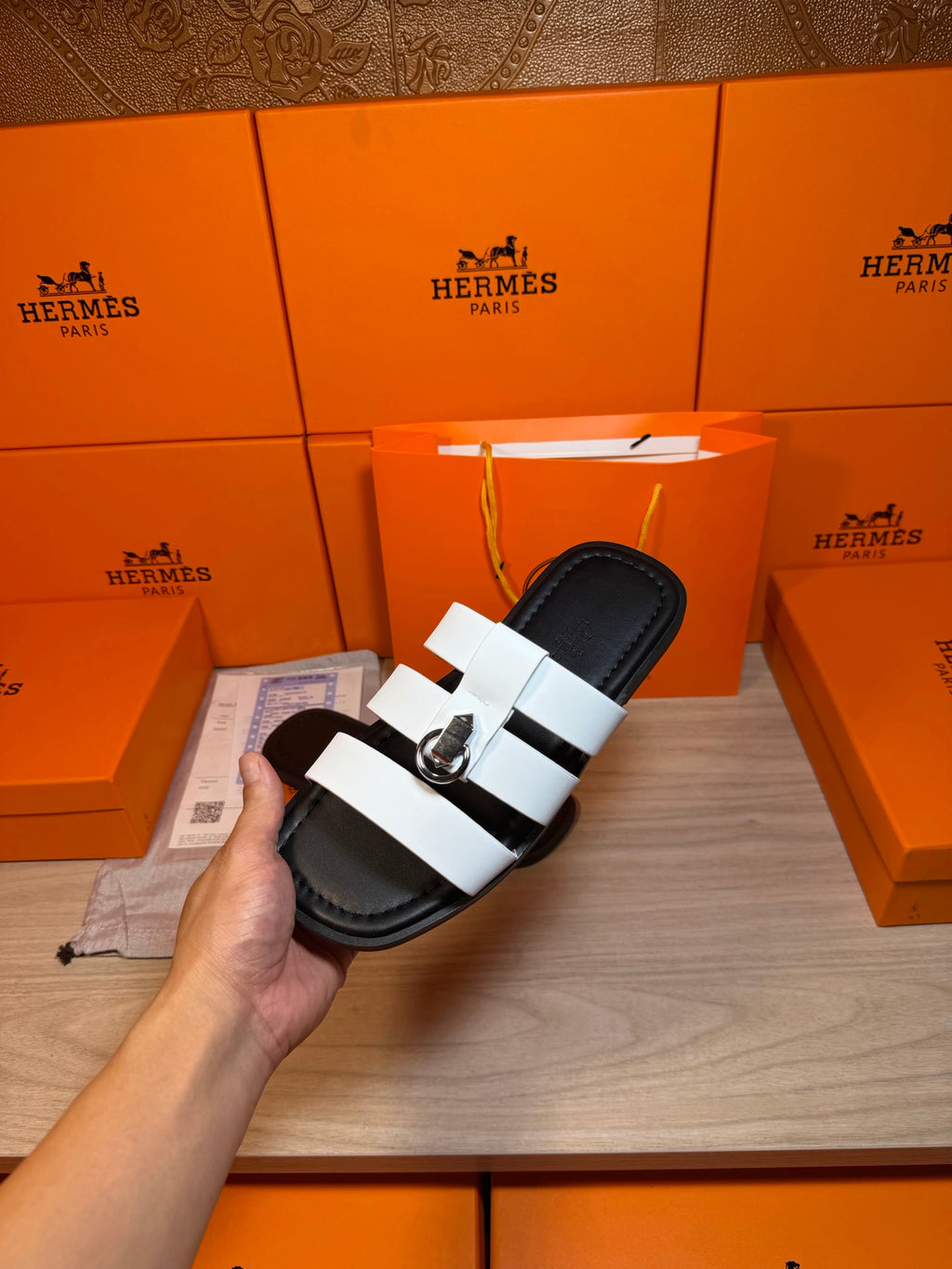 Luxury Hermes sandal held in hand, black footbed with white strap bands and silver buckle.