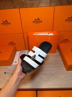 Luxury Hermes sandal held in hand, black footbed with white strap bands and silver buckle.