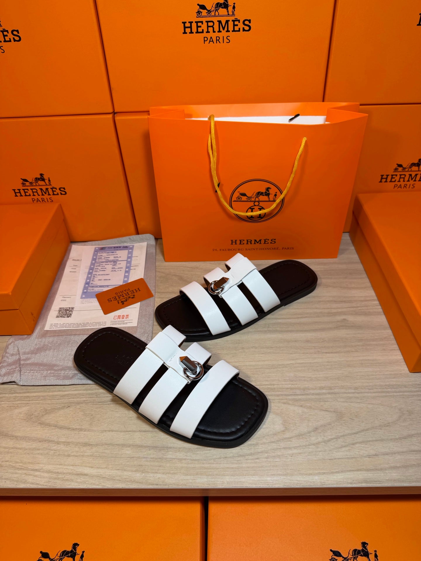 Luxury Hermes sandals with white banded straps and silver buckle, laid on display.