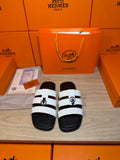 Luxury Hermes sandals with black sole and white leather-look straps, silver buckle.