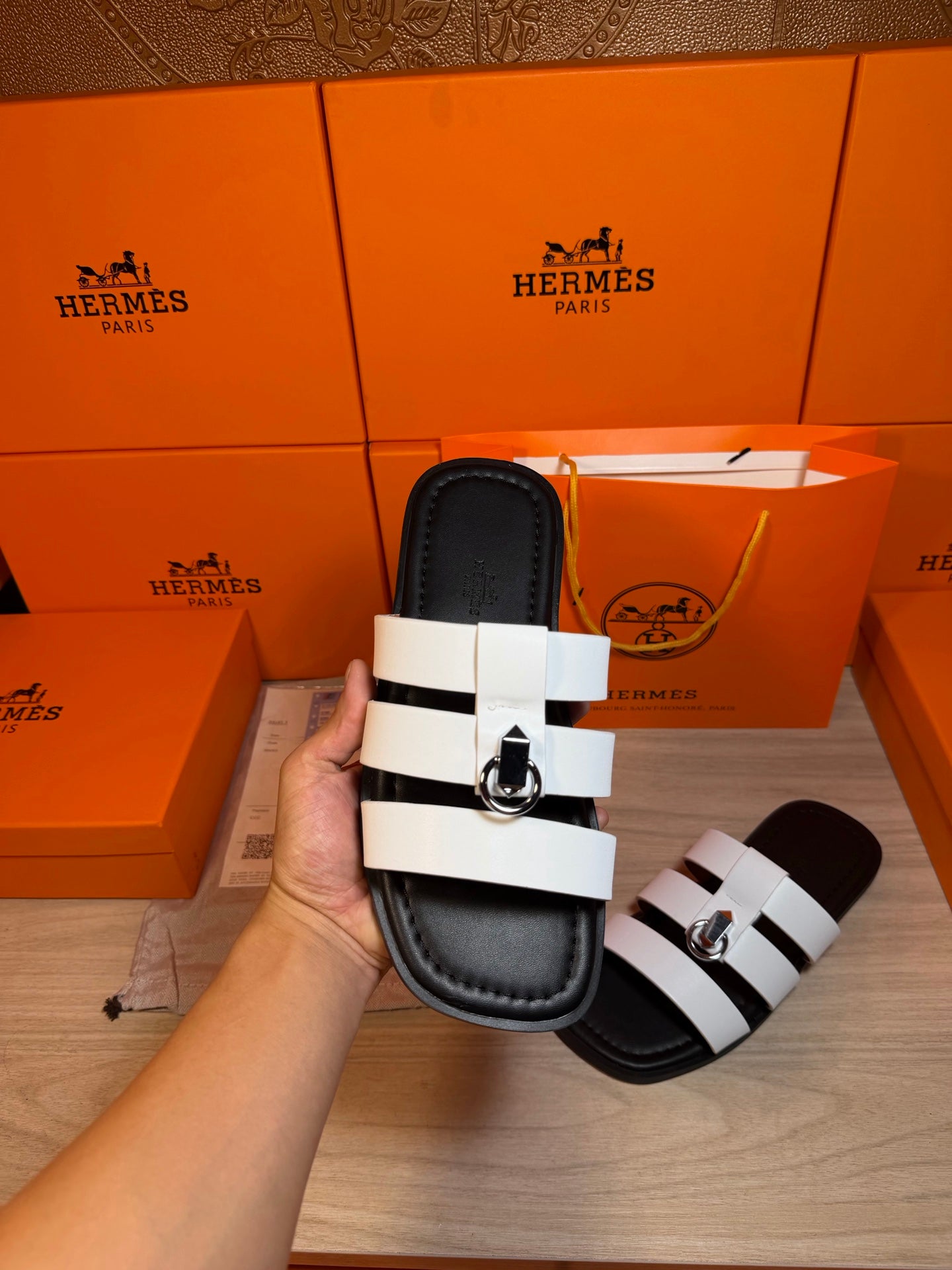 Luxury Hermes sandal held up with two white straps and silver buckle on black sole.
