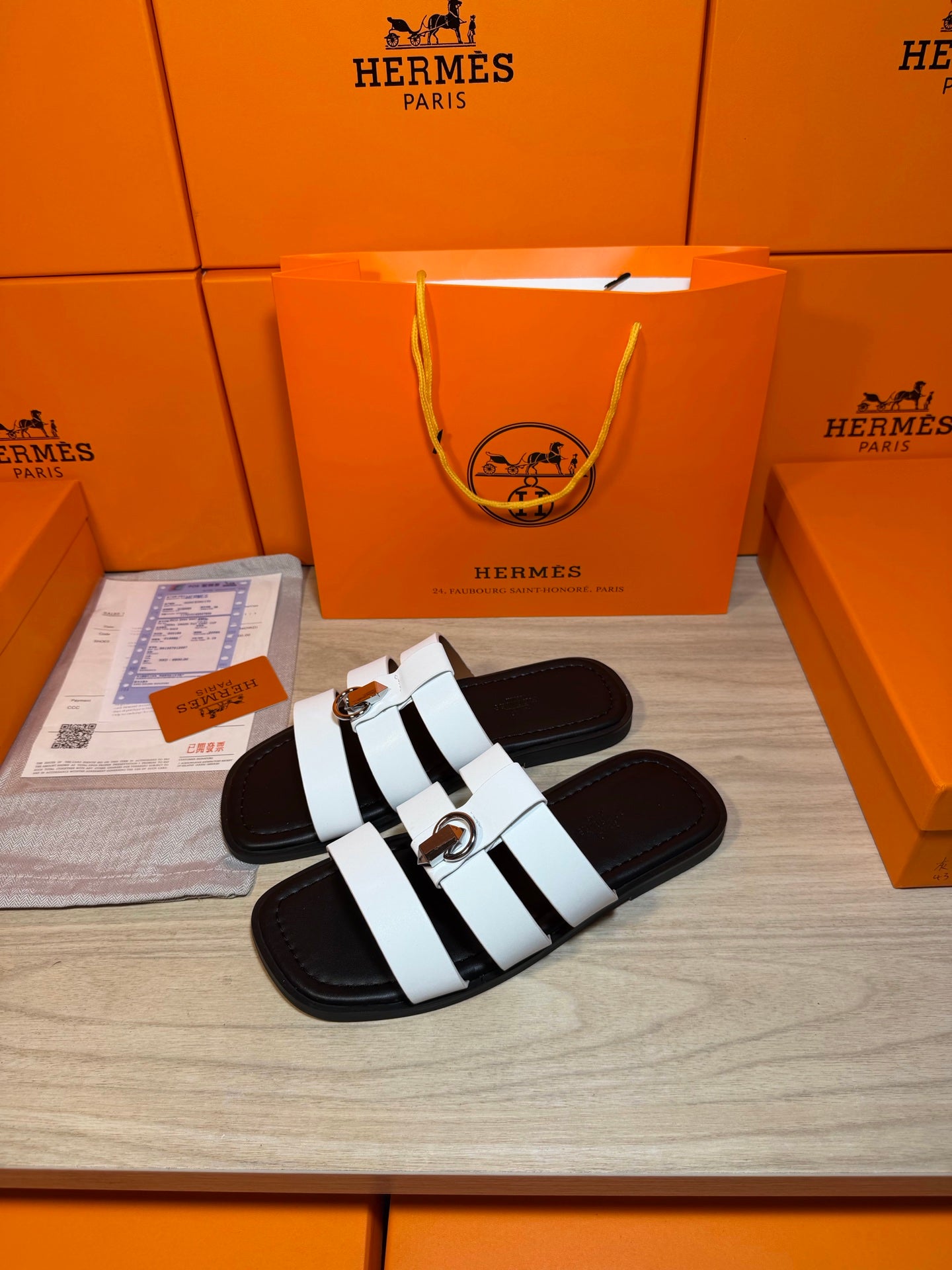 Luxury Hermes sandals, white banded straps on black slides with a silver buckle.