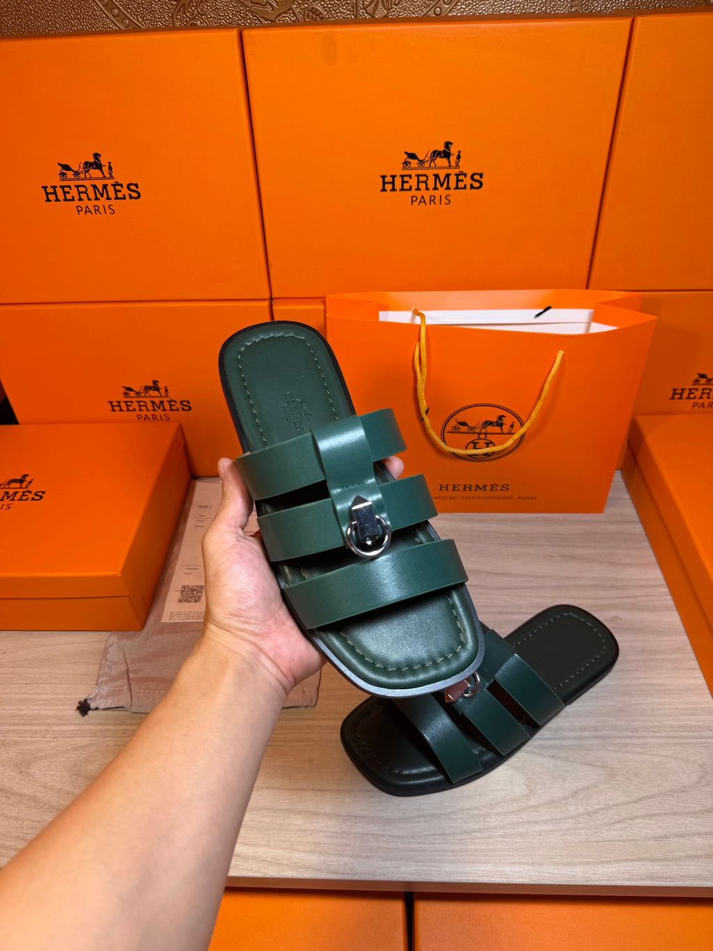 Hand holding teal leather slide sandal with two wide straps and silver buckle